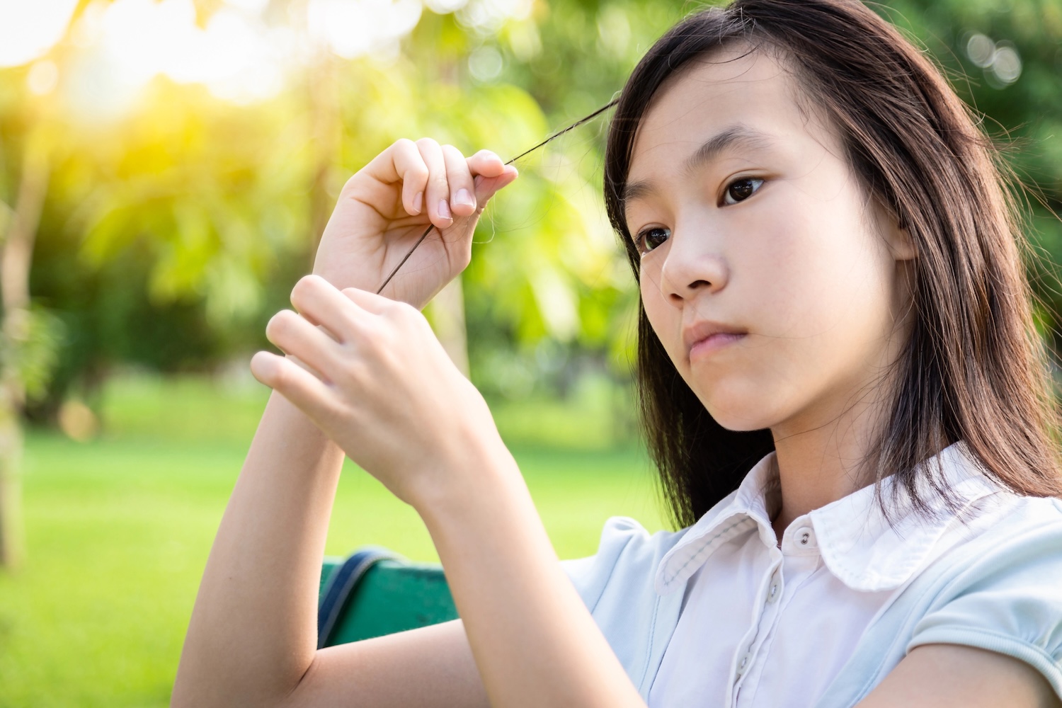 A young girl absently examining a strand of her hair