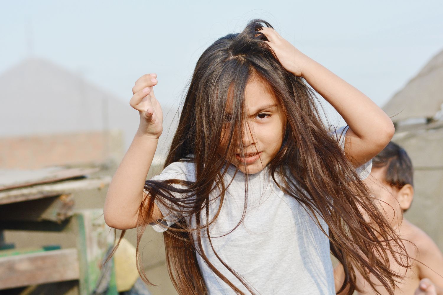 A young girl outdoors with a hand in her hair