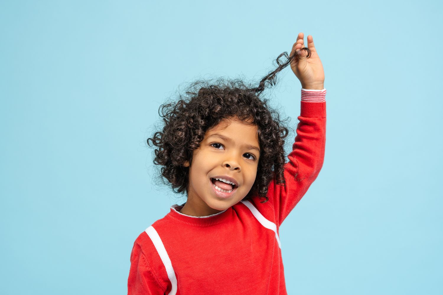 A smiling young child holding up a strand of their curly hair